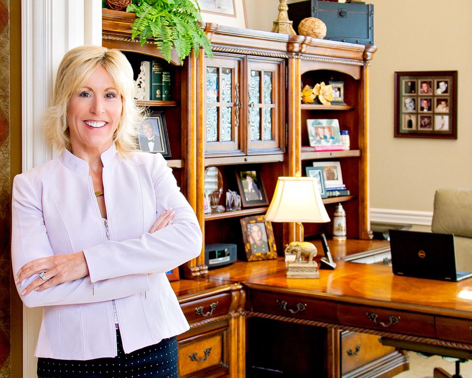 A woman standing in front of a desk with her arms crossed.