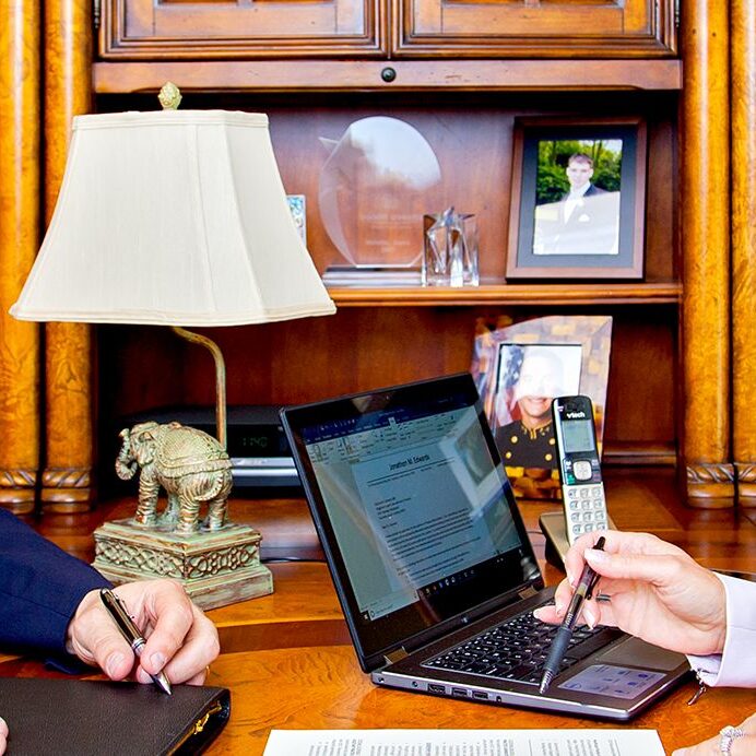 Two people are sitting at a desk with laptops and cell phones.